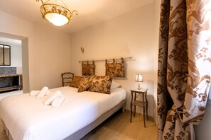 Una cama bien hecha con almohadas y toallas enrolladas, una mesita de noche con lámpara, y una cortina con estampado floral.