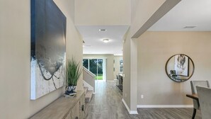 A modern hallway with a wooden console, a large abstract painting, and a round mirror on the wall. - Luxury Lagoon Smart Home in Epperson (Wesley Chapel)