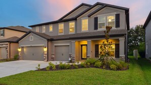 A modern two-story house with a garage, a well-maintained lawn, and a small garden with a decorative plant. - Luxury Lagoon Smart Home in Epperson (Wesley Chapel)