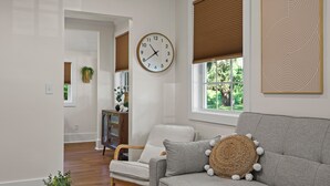 Ein Wohnzimmer mit grauem Sofa, einer runden Uhr und einem Fenster mit Jalousien.