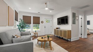 Ein modernes Wohnzimmer mit einem grauen Sofa, einem runden Couchtisch und einem an der Wand befestigten Fernseher.