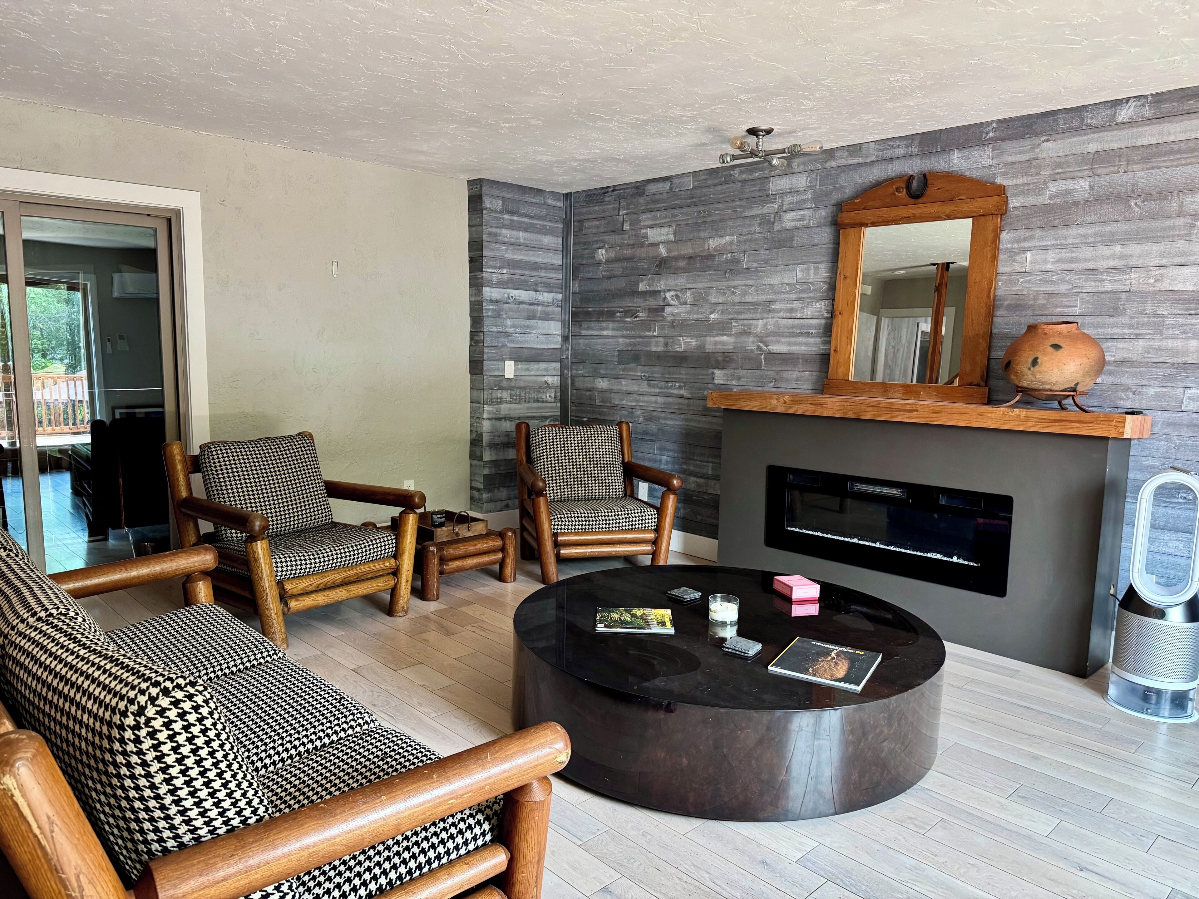 A living room with houndstooth patterned furniture, a fireplace, and a modern ceiling fan.