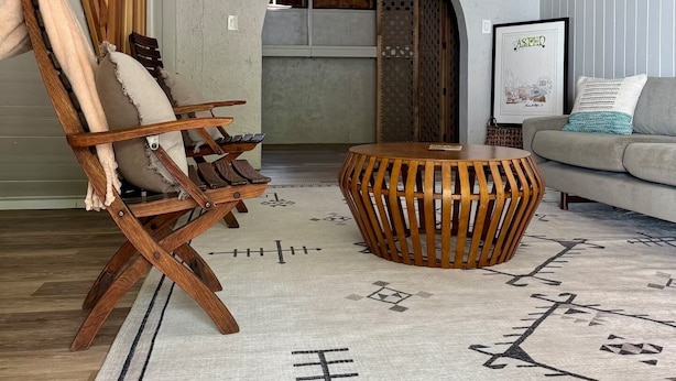 Sala de estar com uma cadeira de madeira, uma mesa de centro redonda e um tapete estampado.