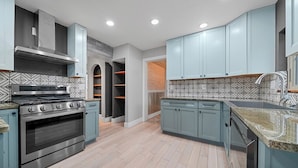 Cozinha moderna com armários azul-claros, fogão de aço inoxidável e azulejos de parede estampados.