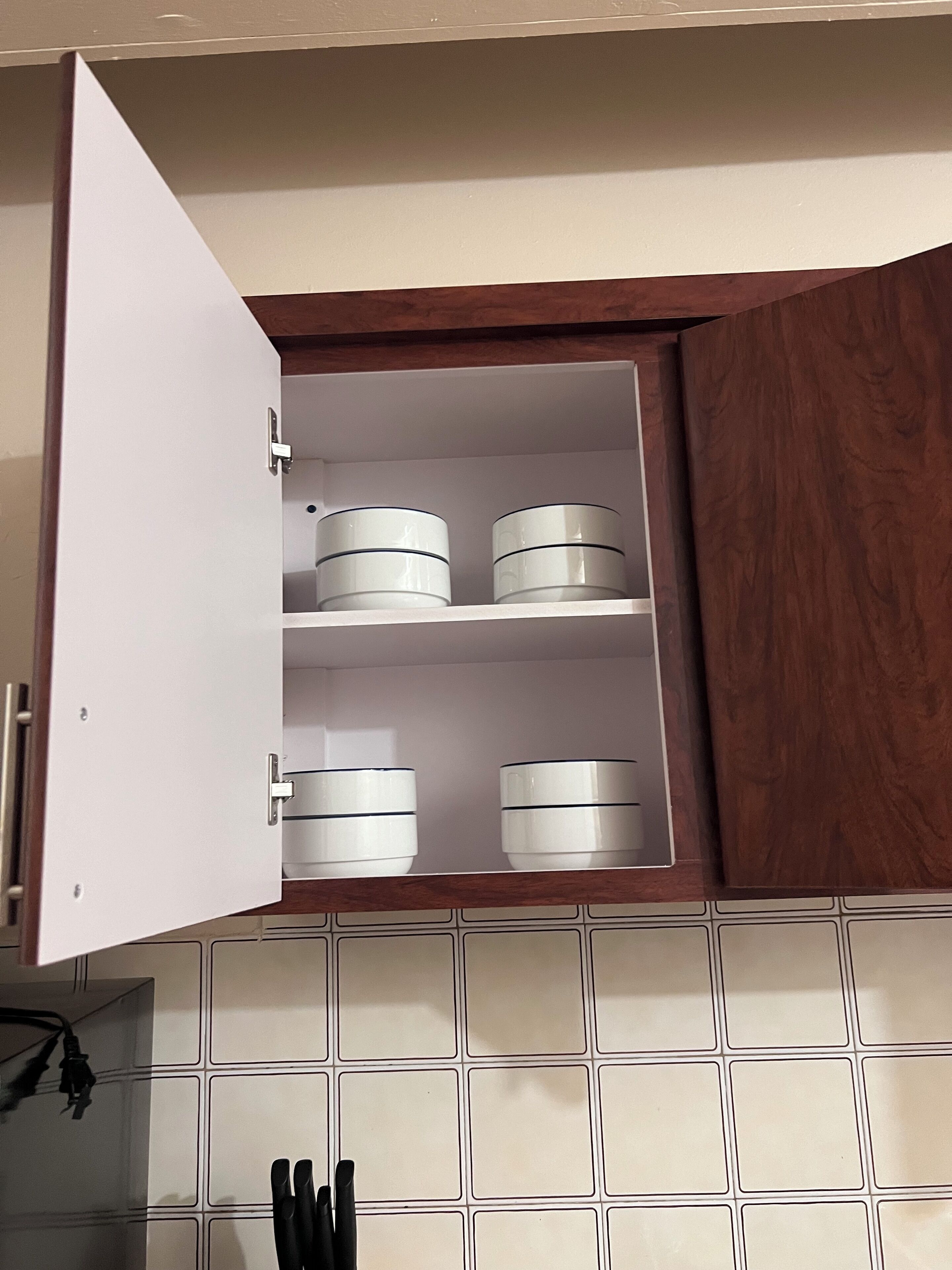 A kitchen with a white cabinet containing three white containers.