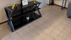 Olohuoneessa on suuri seinälle asennettu taulutelevisio, musta viihdekeskus, jossa on koriste-esineitä, sekä pieni pöytä, jonka päällä on ruukkukasvi.