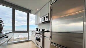 A modern kitchen with a large window, stainless steel appliances, and a view of the city. - Luxe 2 bedroom apartment in Midtown - 24 hour doorman (New York)