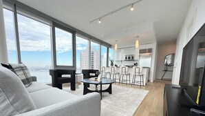 A modern living room with a sofa, a coffee table, and a dining area with chairs and a kitchen in the background. - Luxe 2 bedroom apartment in Midtown - 24 hour doorman (New York)