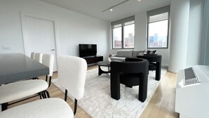 A modern living room with a TV, sofa, and dining area. - Luxe 2 bedroom apartment in Midtown - 24 hour doorman (New York)