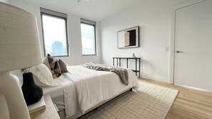 A modern bedroom with a bed, bedside table, and a window with a city view. - Luxe 2 bedroom apartment in Midtown - 24 hour doorman (New York)