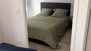 A bedroom with a bed, a nightstand, and a blue chair. - Apartment in quiet residence (Cherbourg-en-Cotentin)