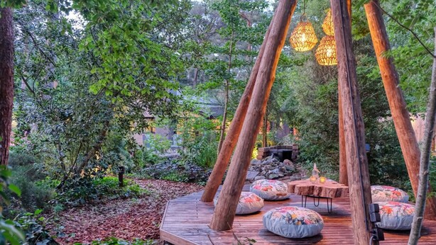 A wooden deck with seating and hanging lights in a forested area.