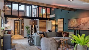 A spacious living area with a high ceiling, a large window, and a cozy seating arrangement.