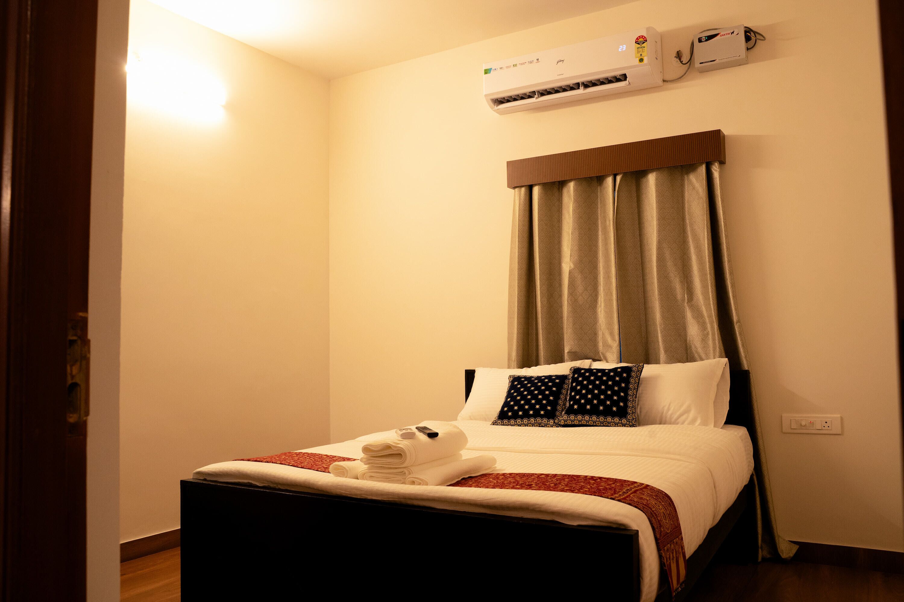 Une chambre d’hôtel équipée d’un lit, d’un appareil de climatisation, d’une fenêtre avec des rideaux et d’une prise électrique au mur.