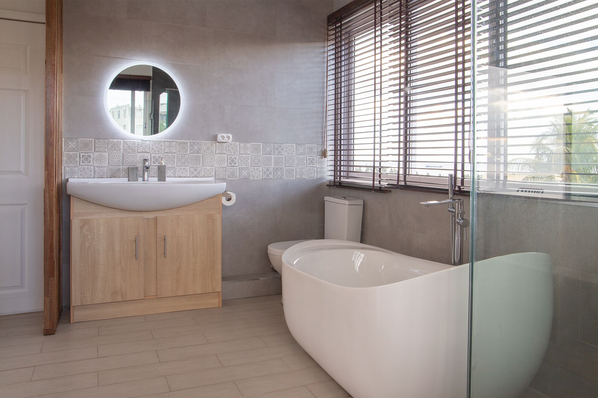 A modern bathroom with a freestanding bathtub, a round mirror, and a toilet.