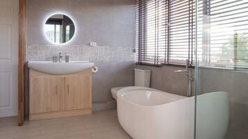 A modern bathroom with a freestanding bathtub, a round mirror, and a toilet.