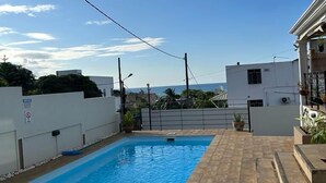 En swimmingpool med flisebelagte kanter, omgivet af en hvid mur og et metalhegn.