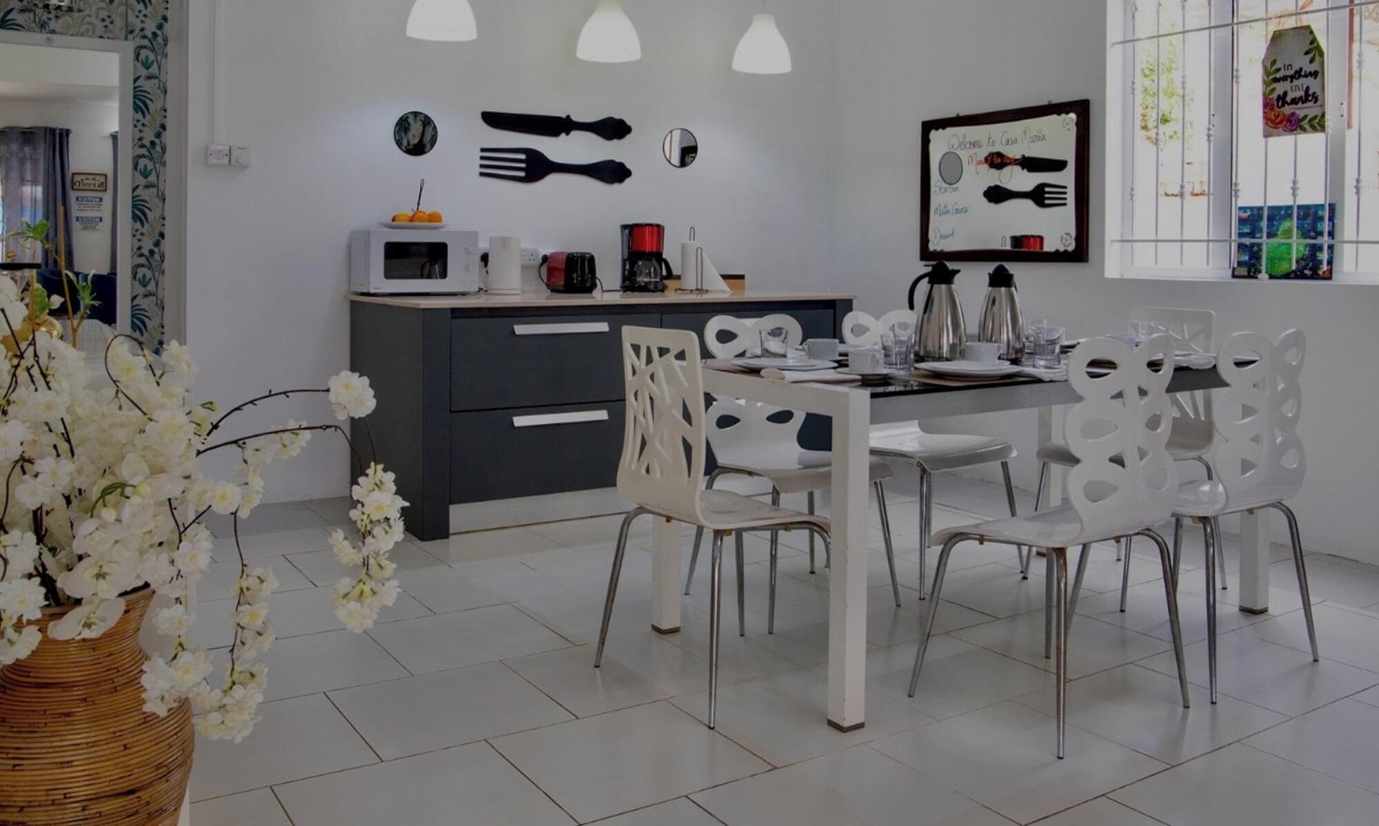 Una cocina moderna con electrodomésticos blancos, una mesa de comedor con sillas blancas y una pared decorativa con utensilios de cocina.