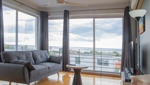 En moderne stue med en grå sofa, et rundt sofabord og udsigt over byen gennem store vinduer.