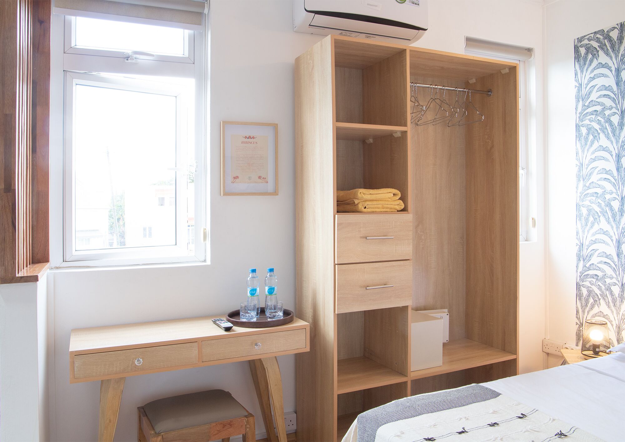 A bedroom with a wooden desk, a wardrobe, a shower, and a bed with a patterned bedspread.