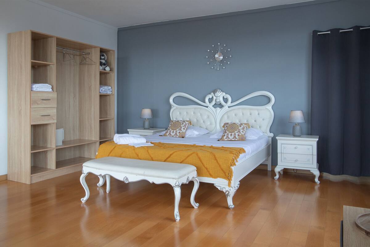 Un dormitorio con un armario grande, una cama con cabecero blanco, dos mesitas de noche y un reloj de pared.