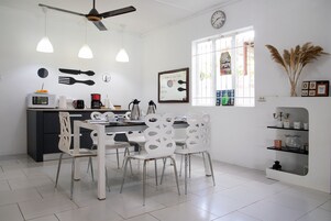 Una cocina moderna con armarios blancos, una mesa de comedor con sillas blancas, un ventilador de techo y un ventanal con detalles decorativos.