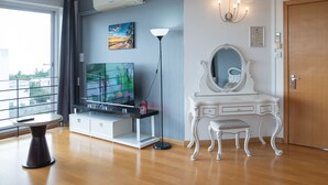 Een kamer met een grote flatscreen-tv, een witte kaptafel met spiegel, een vloerlamp en een deur.