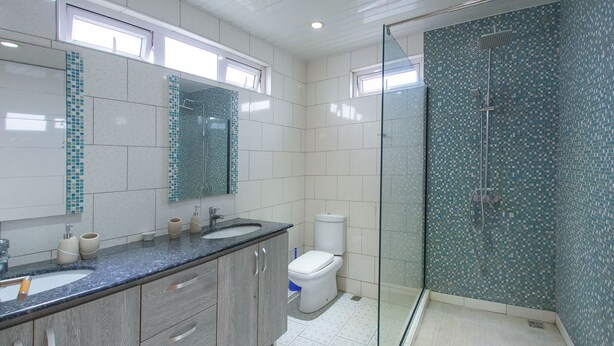 A modern bathroom with a glass-enclosed shower, a large mirror, and a sink with a granite countertop. - Casa Maria (Pointe aux Sables)