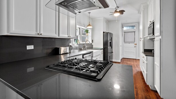 Una cocina moderna con armarios blancos, encimera negra, electrodomésticos de acero inoxidable y ventilador de techo.