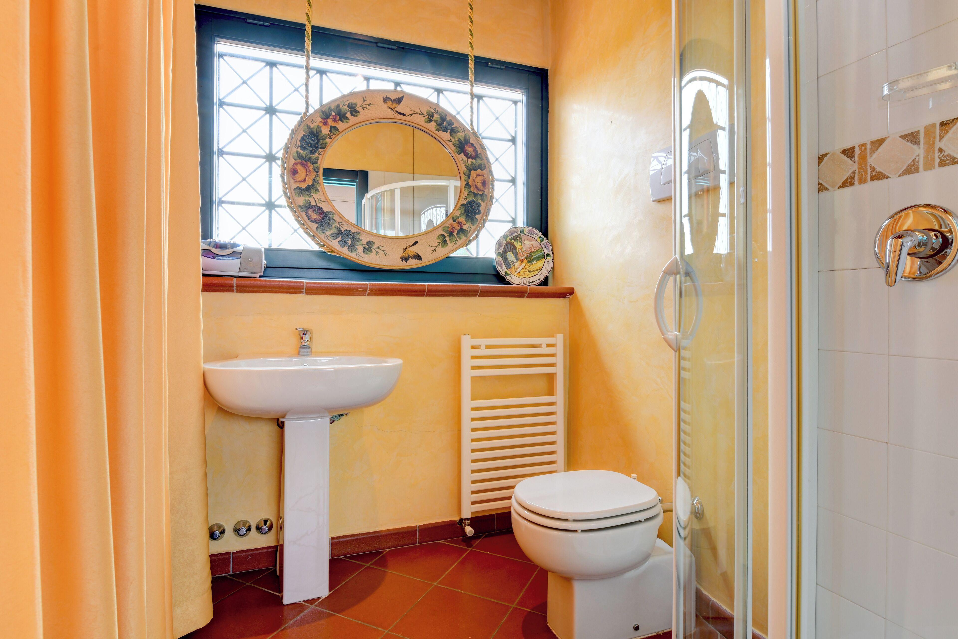 Une salle de bain équipée d’un lavabo, de toilettes et d’une fenêtre agrémentée d’un miroir décoratif.