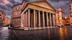 Edifici clàssic amb columnes i frontó, envoltat de carrers empedrats i altres edificis.