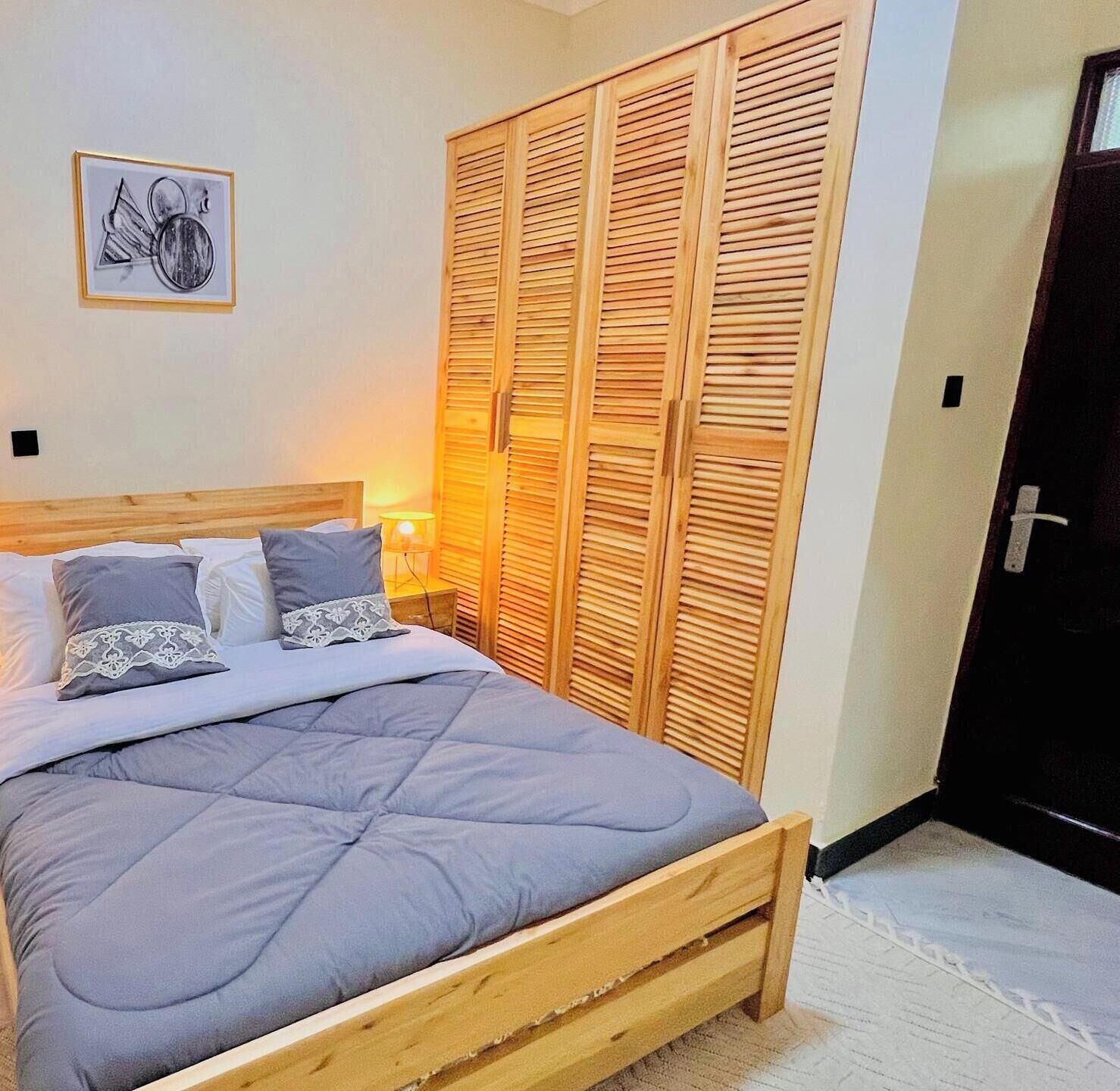A bedroom with a wooden bed, a nightstand, a wall-mounted lamp, and a wardrobe with louvered doors.