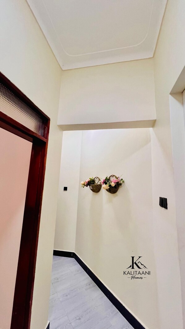 A hallway with a white wall, a wooden door frame, and a logo for 'KALITAANI Homes'.