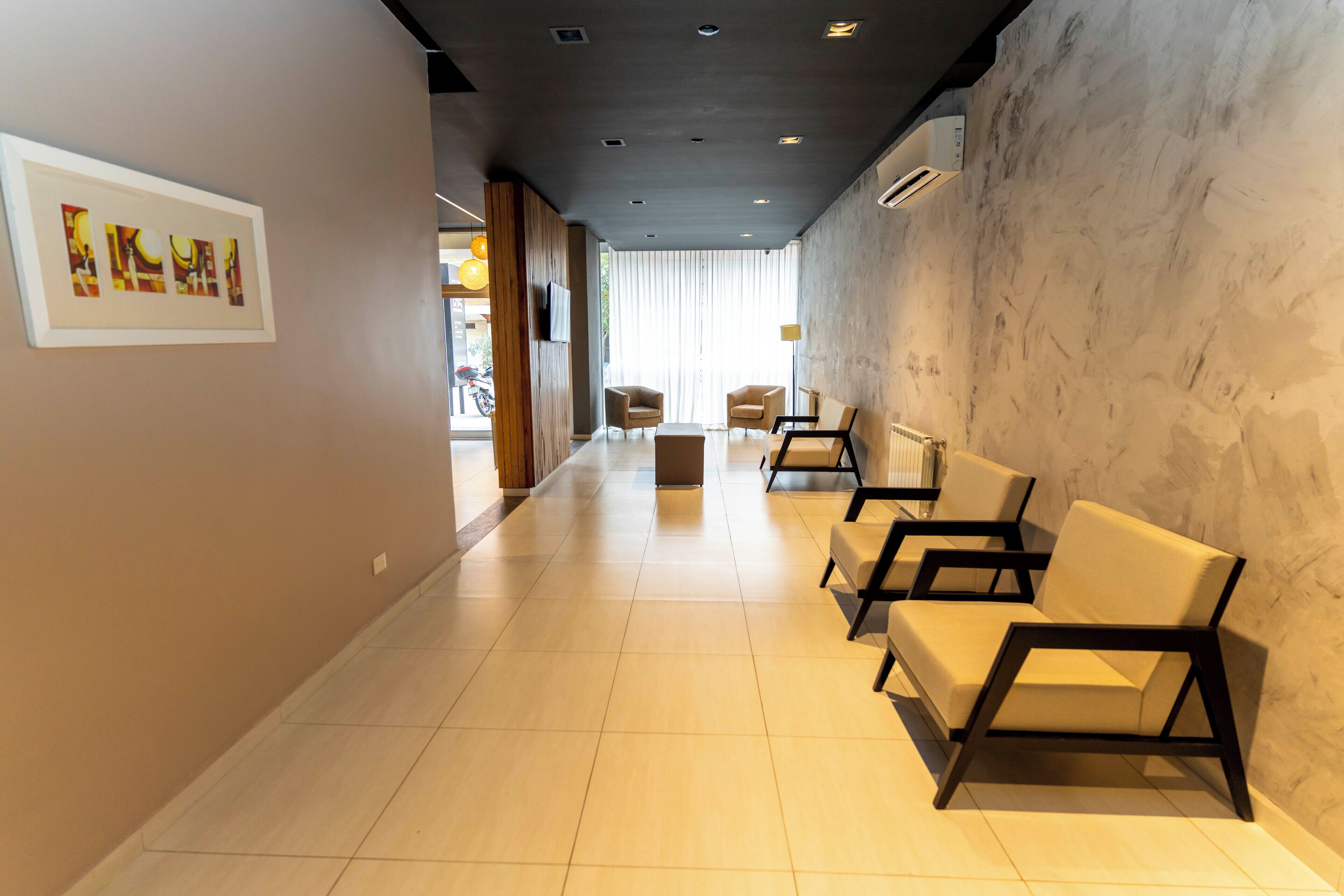 A hotel lobby with a long corridor, beige chairs, a framed artwork on the wall, and a large window with curtains.