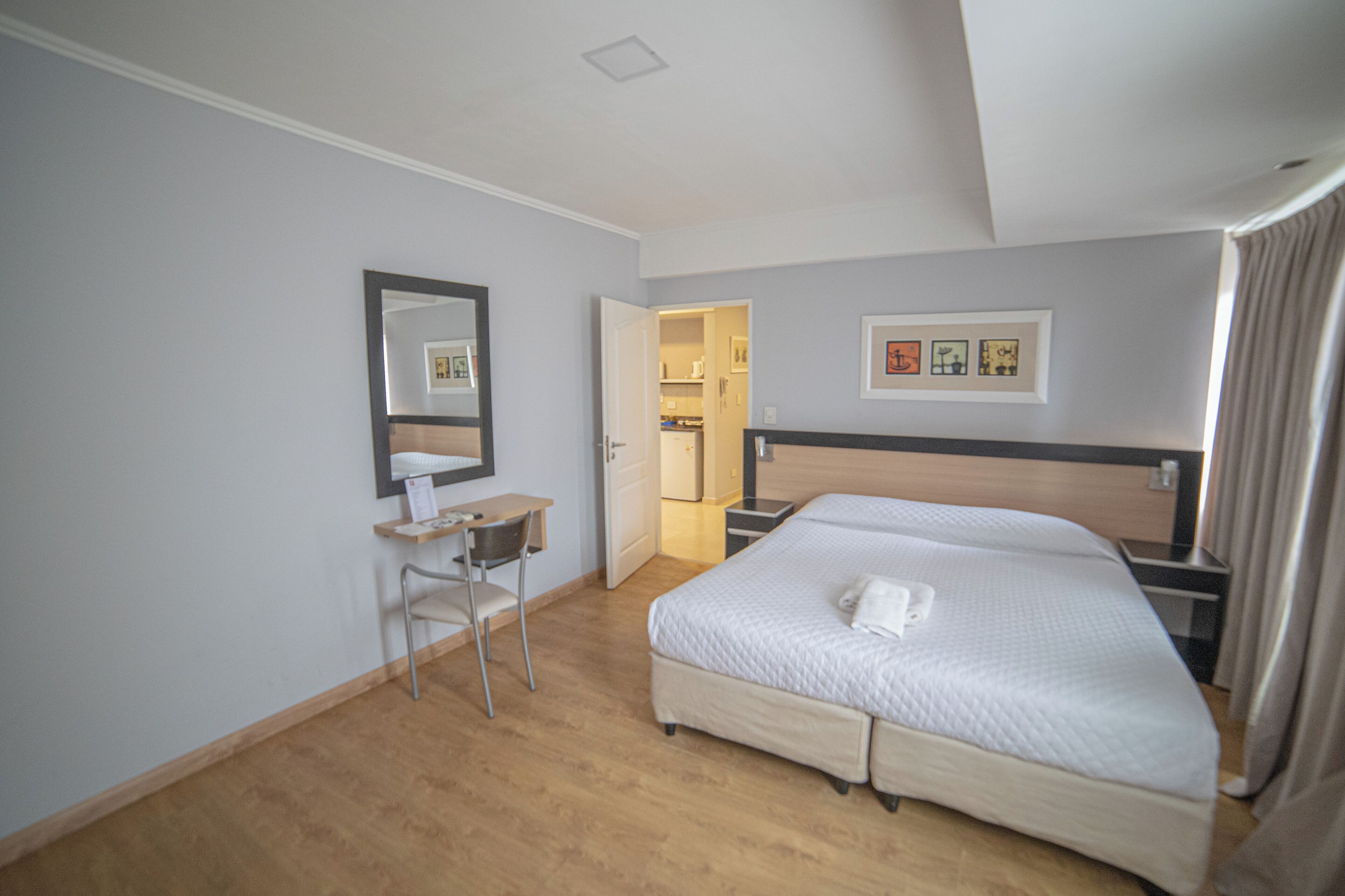 Habitación de hotel con cama, escritorio, silla, espejo y puerta que da a un baño.
