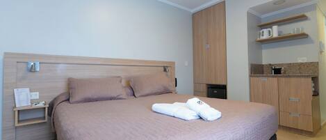 A hotel room with a bed, a nightstand, a wardrobe, and a kitchenette area.