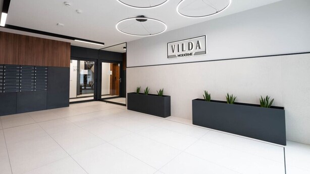 Un área de recepción moderna con diseño minimalista, que incluye un mostrador, tres lámparas colgantes y un cartel en la pared.