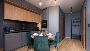 Una cocina moderna con armarios grises oscuros, una encimera de mármol y un estante de madera. Hay una mesa de comedor con cuatro sillas y un pequeño florero con flores.