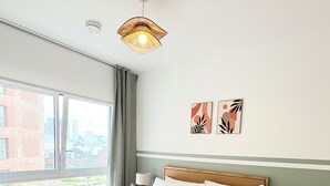 Ein ordentlich bezogenes Bett mit Holz-Kopfteil, ein Nachttisch mit Lampe und Blick ins Grüne.