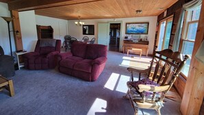 A cozy living room with a wooden ceiling, a red sofa, a wooden chair, and a dining table. - Charming 3-bedroom cabin in beautiful Boomer with AC (Boomer)