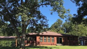 A brick building with a covered porch, surrounded by trees and a grassy lawn. - Charming 3-bedroom cabin in beautiful Boomer with AC (Boomer)