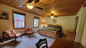 A bedroom with a bed, two chairs, a wooden table, a ceiling fan, and a window. - Charming 3-bedroom cabin in beautiful Boomer with AC (Boomer)