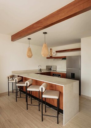 Une cuisine moderne dotée d’un îlot central, de tabourets de bar, de luminaires suspendus et d’un réfrigérateur en acier inoxydable.