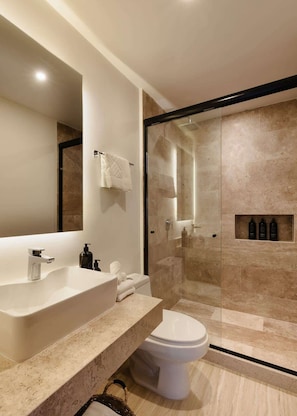 Un baño moderno con un espejo grande, un lavamanos blanco, un inodoro y una ducha con mampara de vidrio.