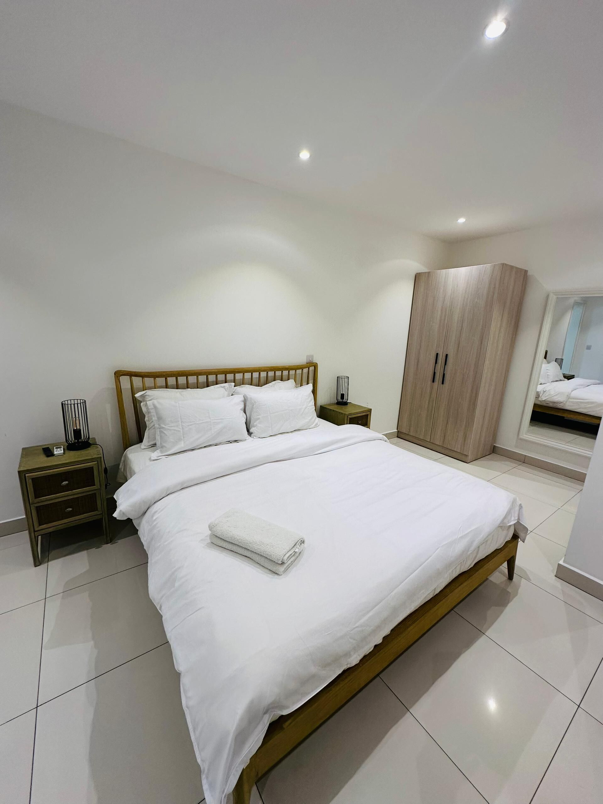 A modern bedroom with a wooden bed, white bedding, a nightstand with a lamp, and a wardrobe.
