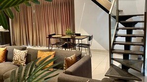 A modern living room with a grey sofa set, a dining table with chairs, and a staircase leading to an upper level. - premier luxury apartment (Accra)