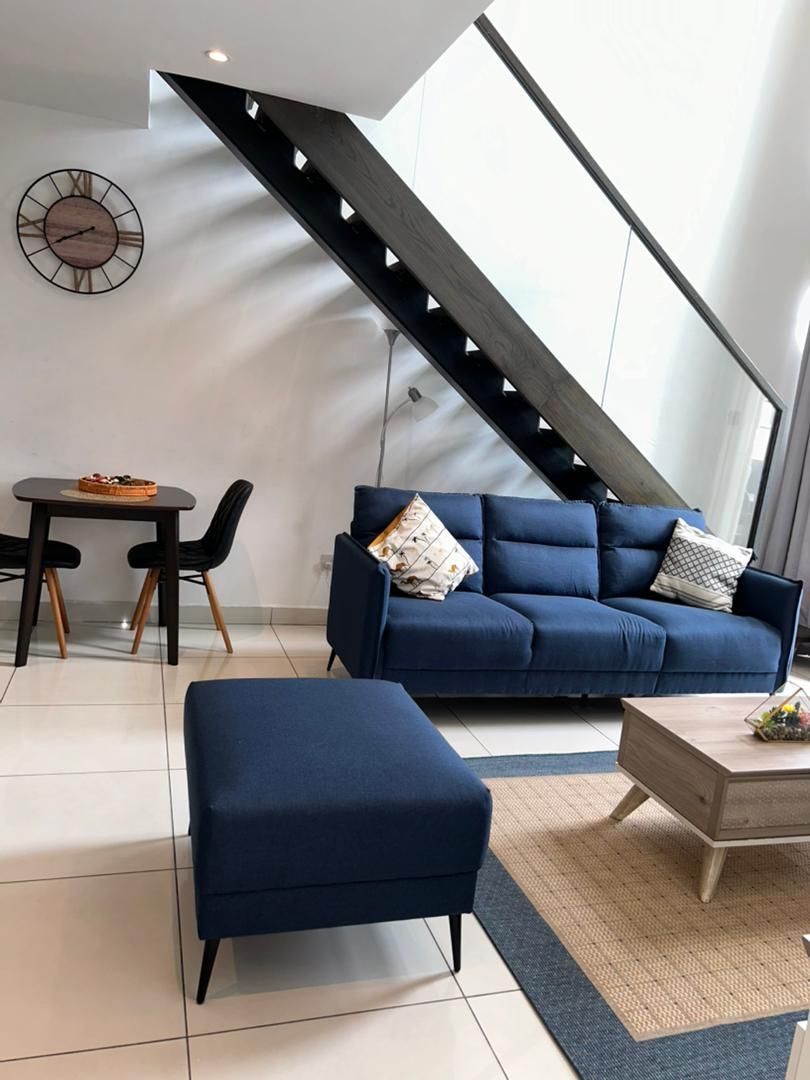 A modern living room with a blue sofa, an ottoman, a coffee table, and a dining area with a small table and chairs.