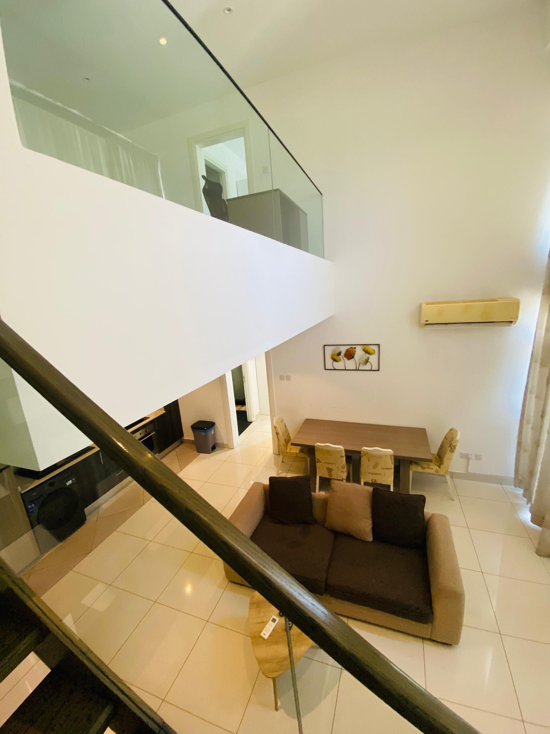 A modern living room with a glass staircase, a sofa set, and a dining area.