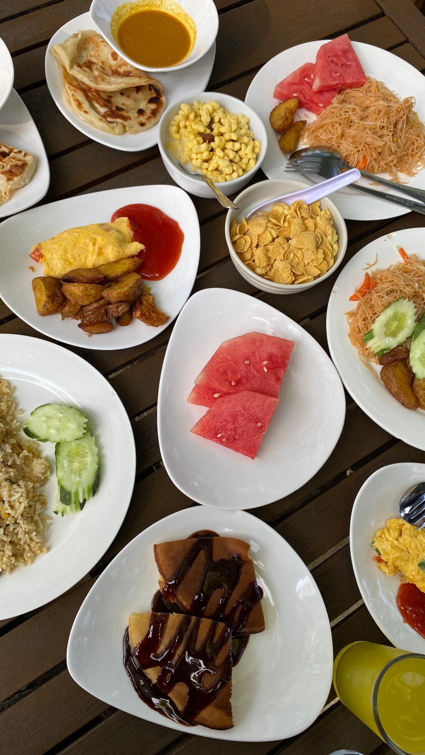 Diversos pratos, incluindo arroz, frituras e fatias de melancia, sobre uma mesa.