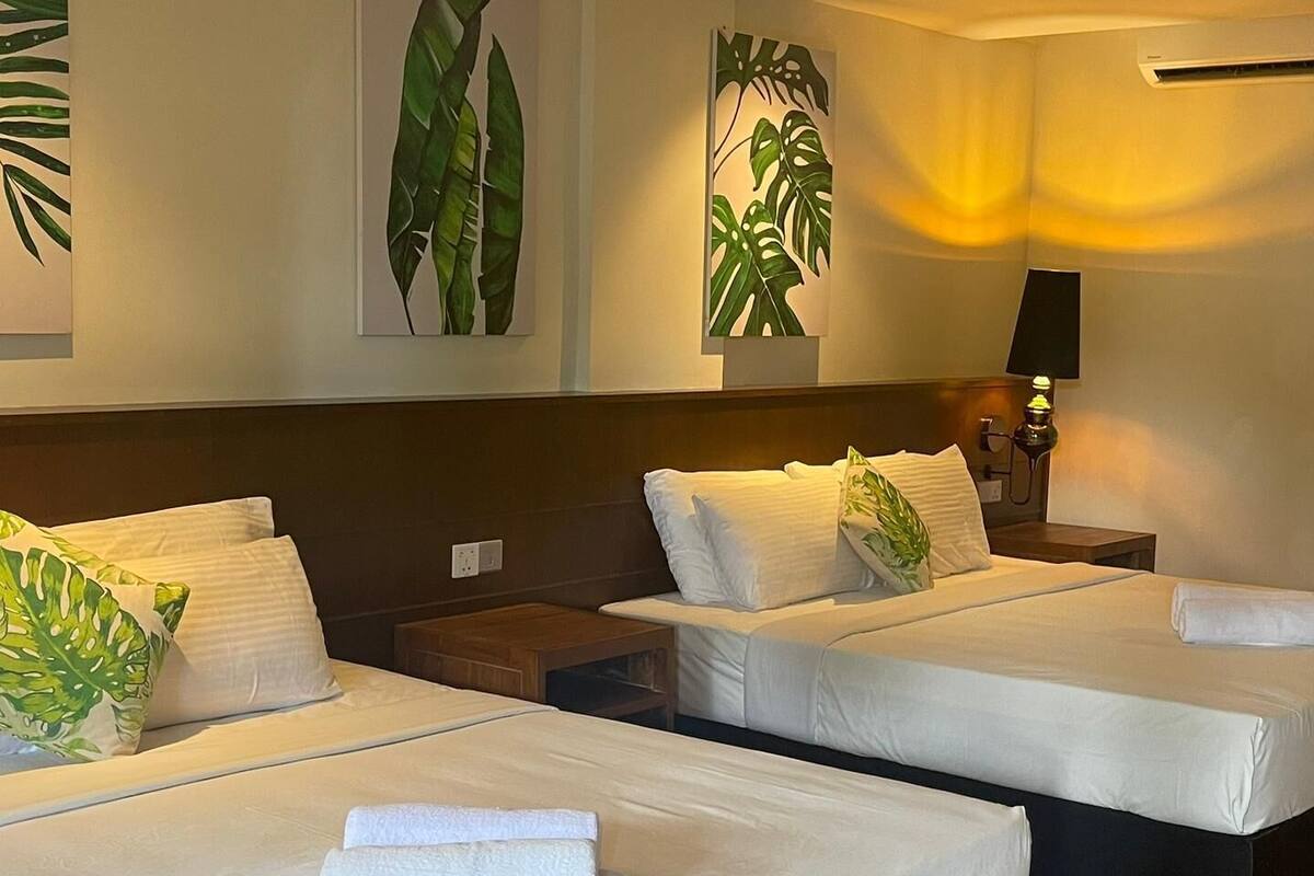 A hotel room with two beds, wooden flooring, and wall-mounted air conditioning.